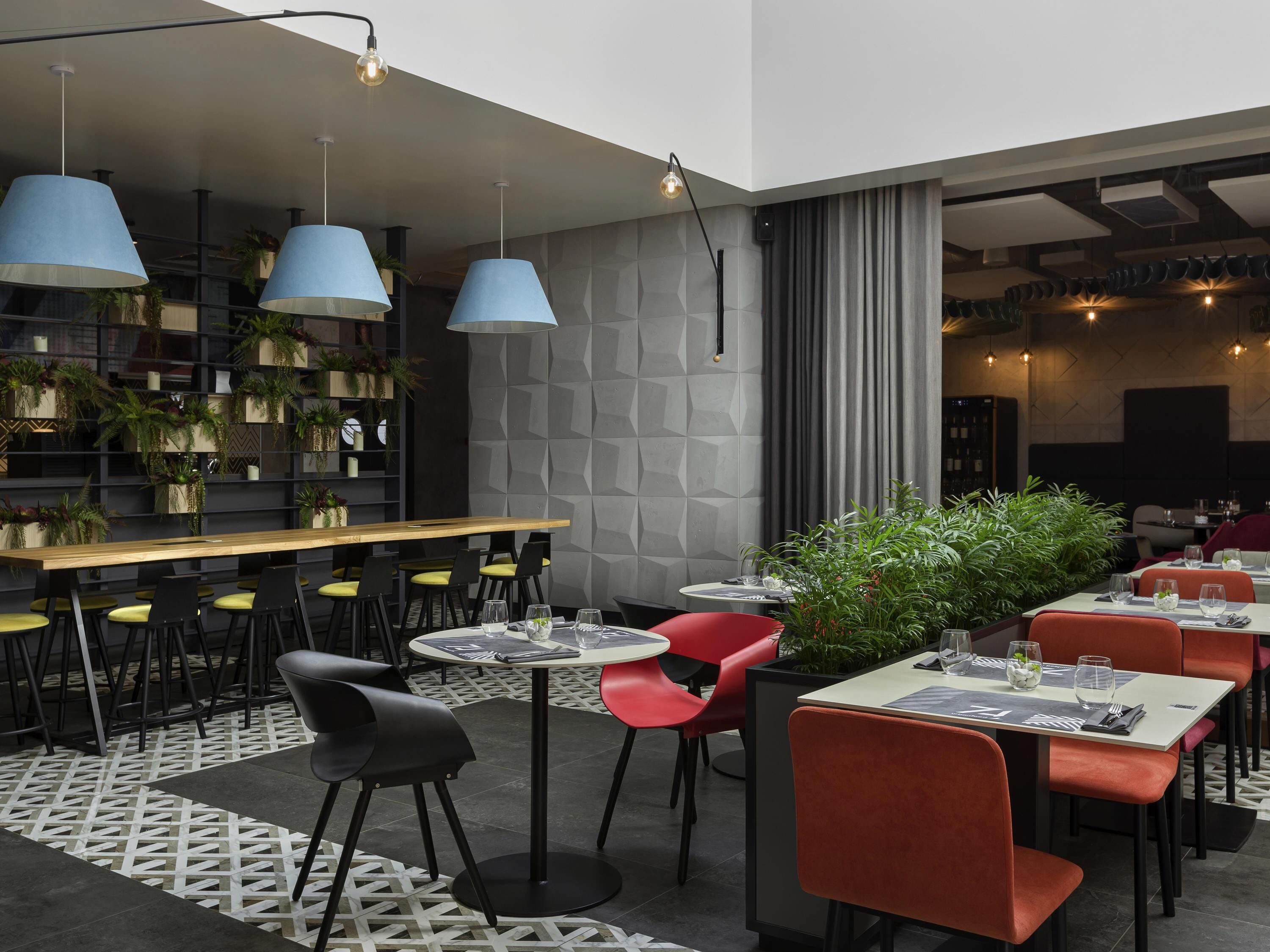 A modern restaurant with a bar area, multiple seating arrangements, and decorative plants.