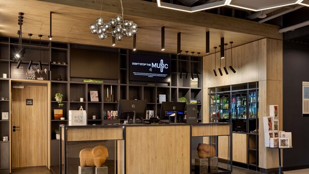A modern bar area with wooden accents, a digital screen displaying 'DON'T STOP THE MUSIC', and a bar counter with HP computers. - Ibis Kyiv Beresteiska (Kyiv)