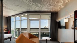 A modern hotel room with large windows, a curved sofa, a small round table, and a TV mounted on the wall. - Ibis Kyiv Beresteiska (Kyiv)
