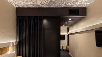 A hotel room with a bed, a small table, a chair, a TV, and a dark curtain.