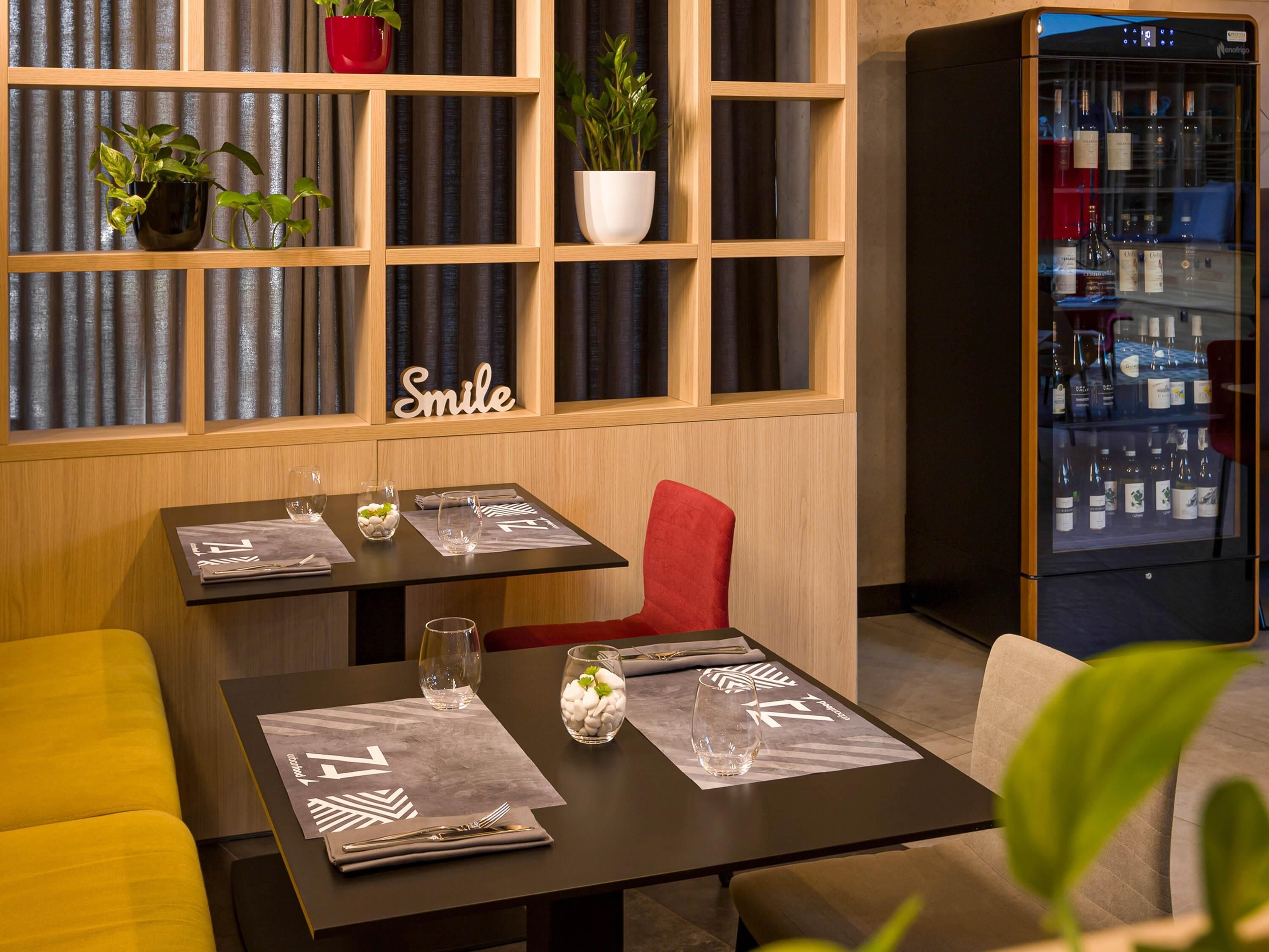 Un restaurante con estantes de madera, un enfriador de vinos y una mesa con un mantel individual, vaso y un jarrón con flores.