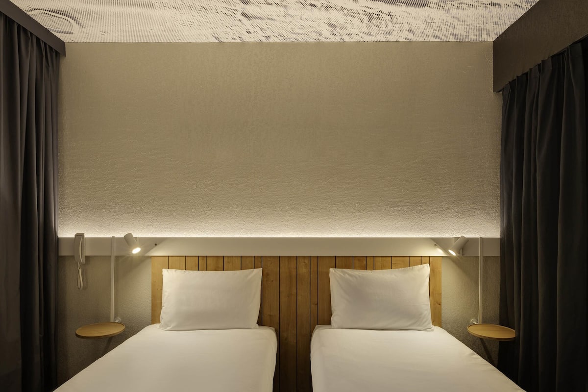 Ein Hotelzimmer mit zwei Betten, einem Holzkopfende, Nachttischen und einer Decke mit Struktur.