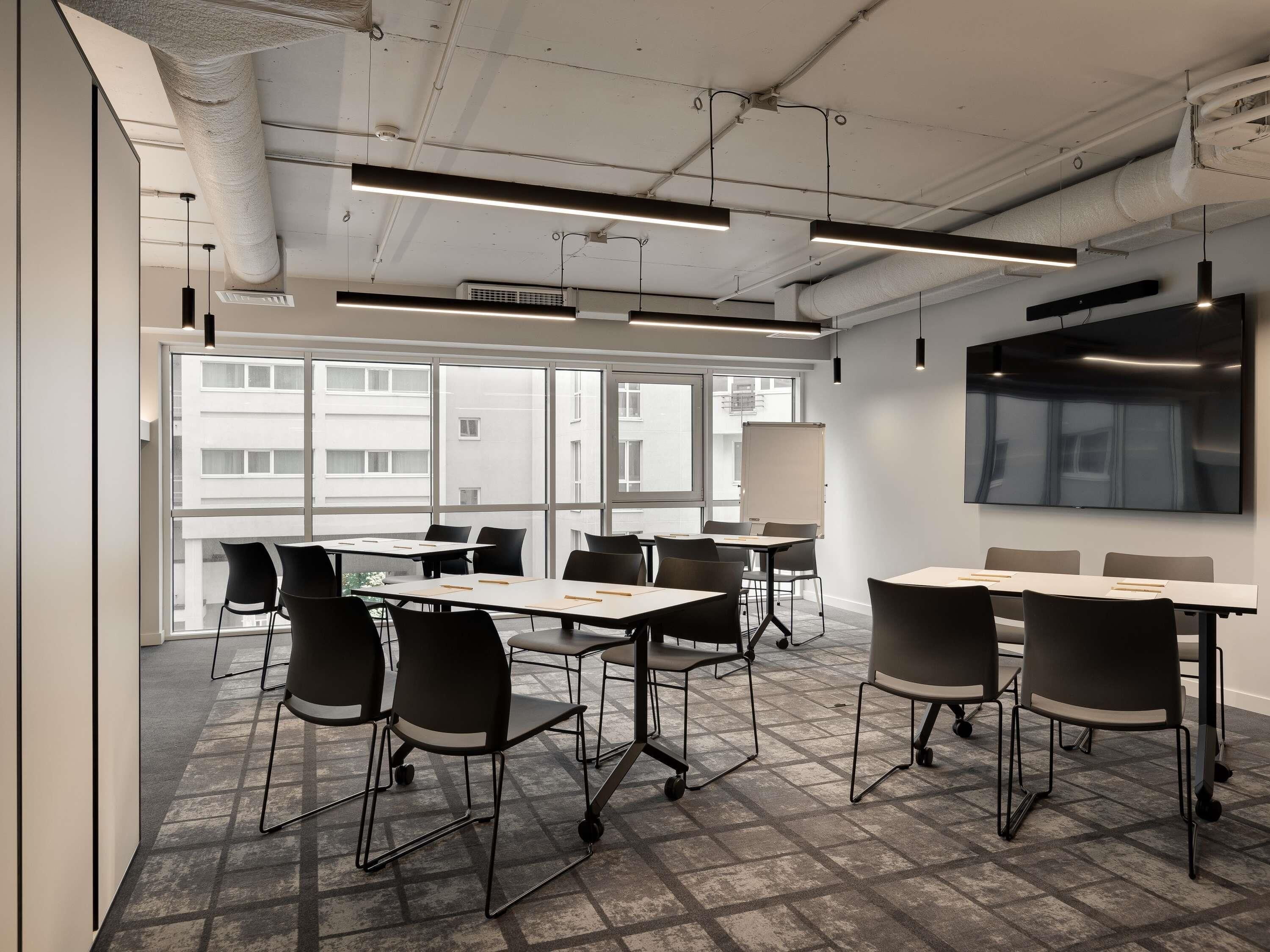 Une salle de conférence moderne équipée de tables, de chaises, d’un grand téléviseur à écran plat et d’un tableau blanc.