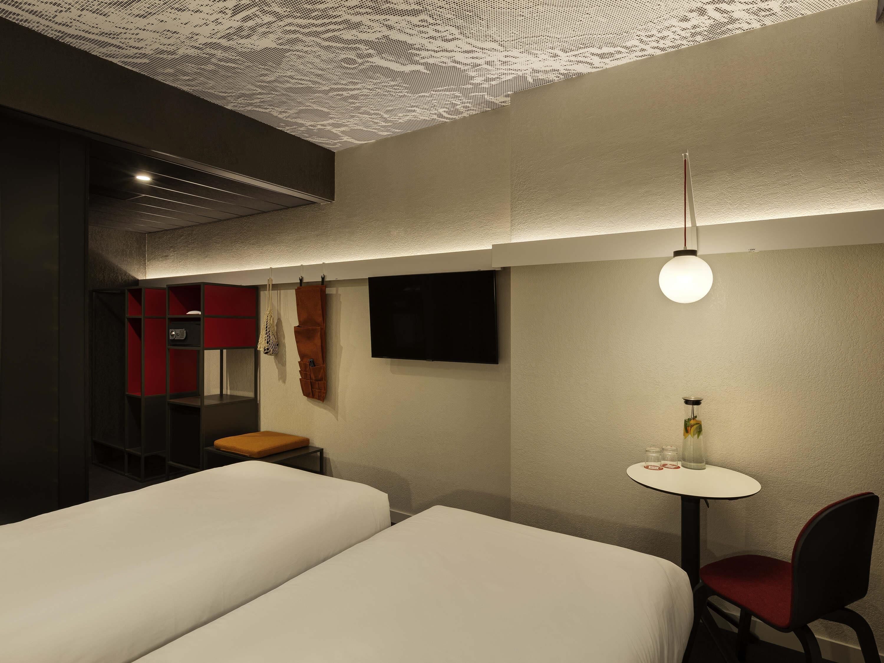 Ein Hotelzimmer mit zwei Betten, einem kleinen Tisch mit Stuhl, einem Fernseher und einem besonderen Deckenstil.