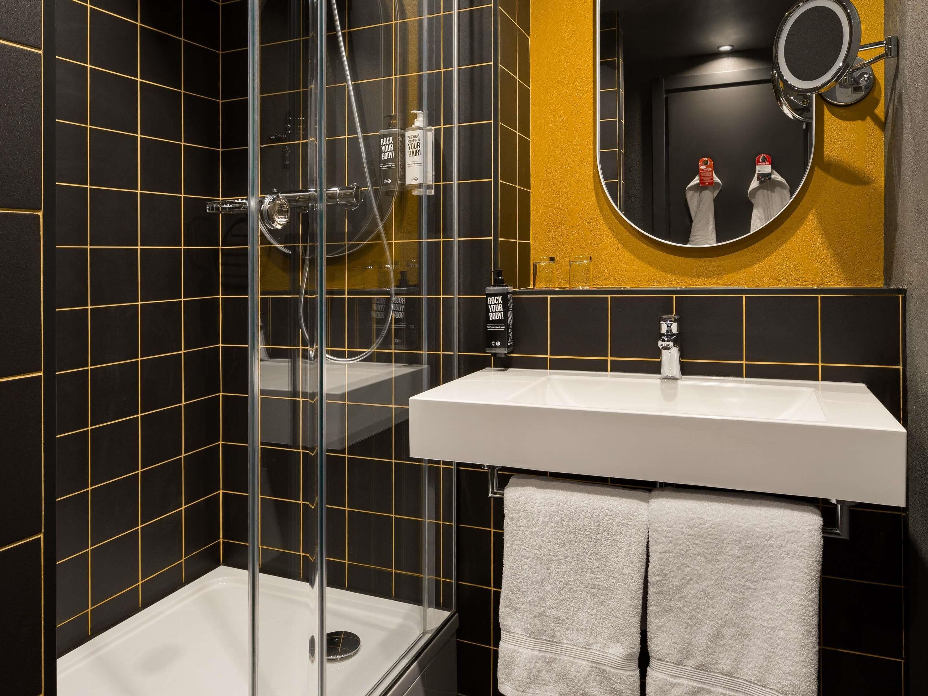 Un baño con ducha envuelta en vidrio, un lavamanos blanco y un espejo.