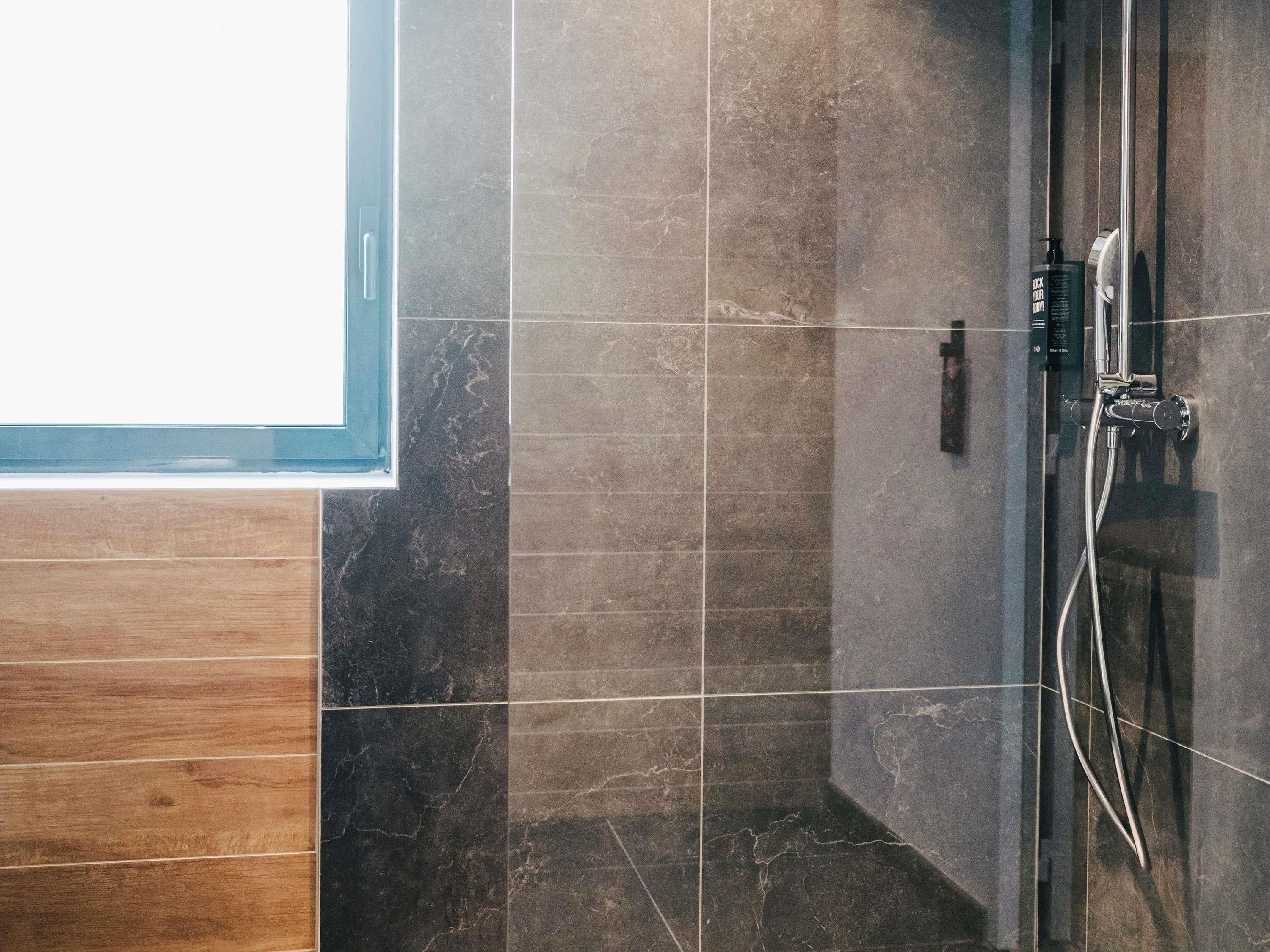 A shower area with a glass door, tiled walls, and a wooden panel on the left.