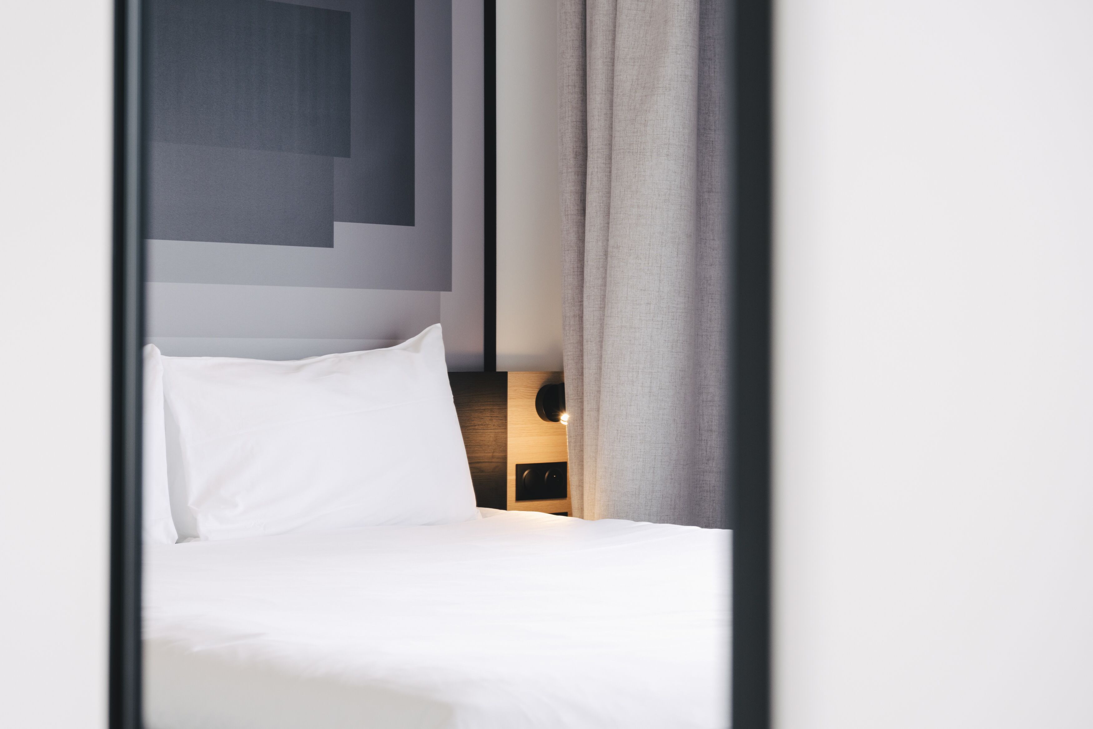 A neatly made bed with white linens and a headboard with a geometric design.