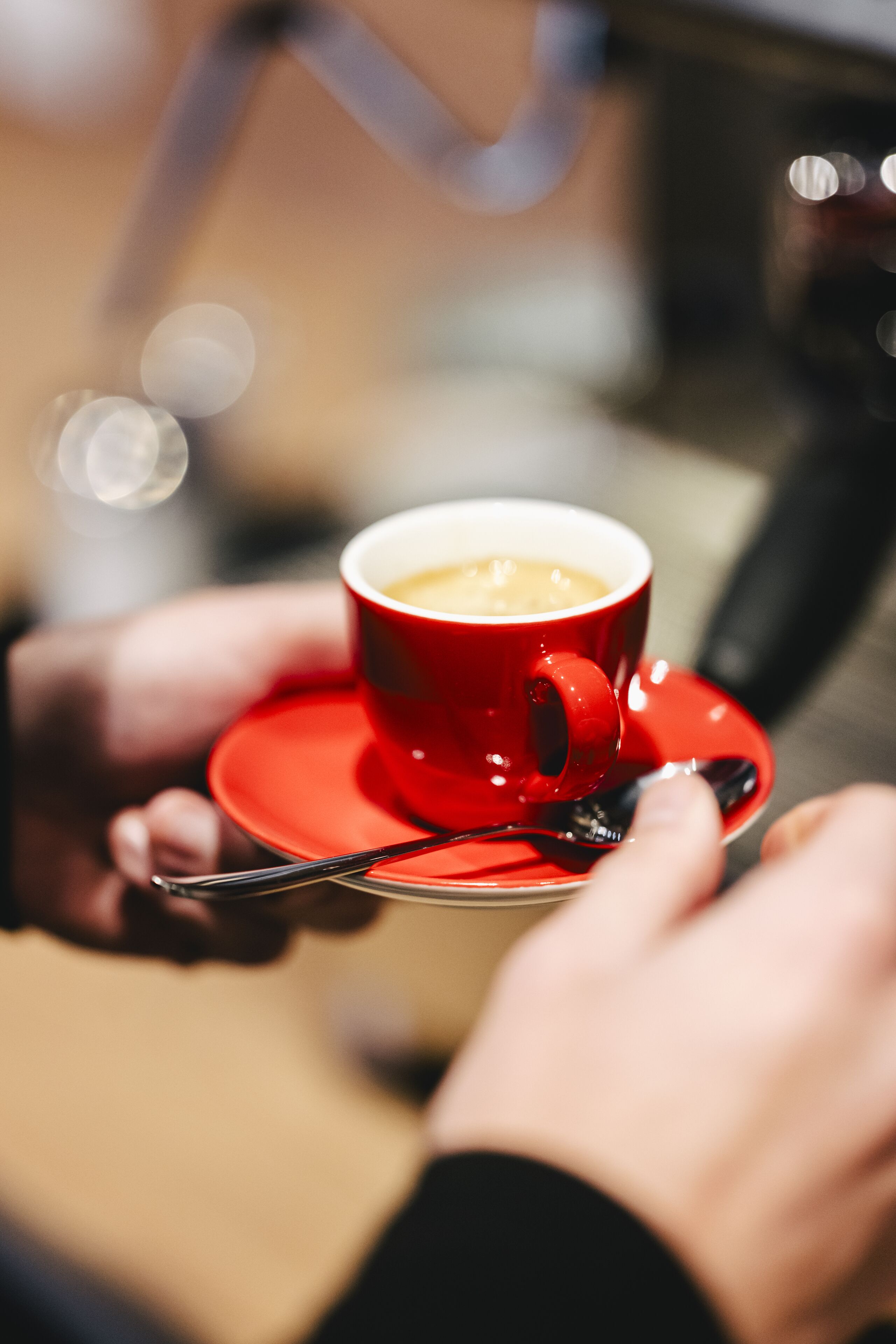 Um close-up de uma chávena vermelha com café sobre um pires, sendo segurada por uma pessoa.