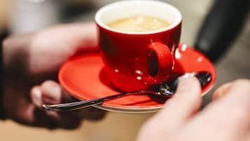 Um close-up de uma chávena vermelha com café sobre um pires, sendo segurada por uma pessoa.