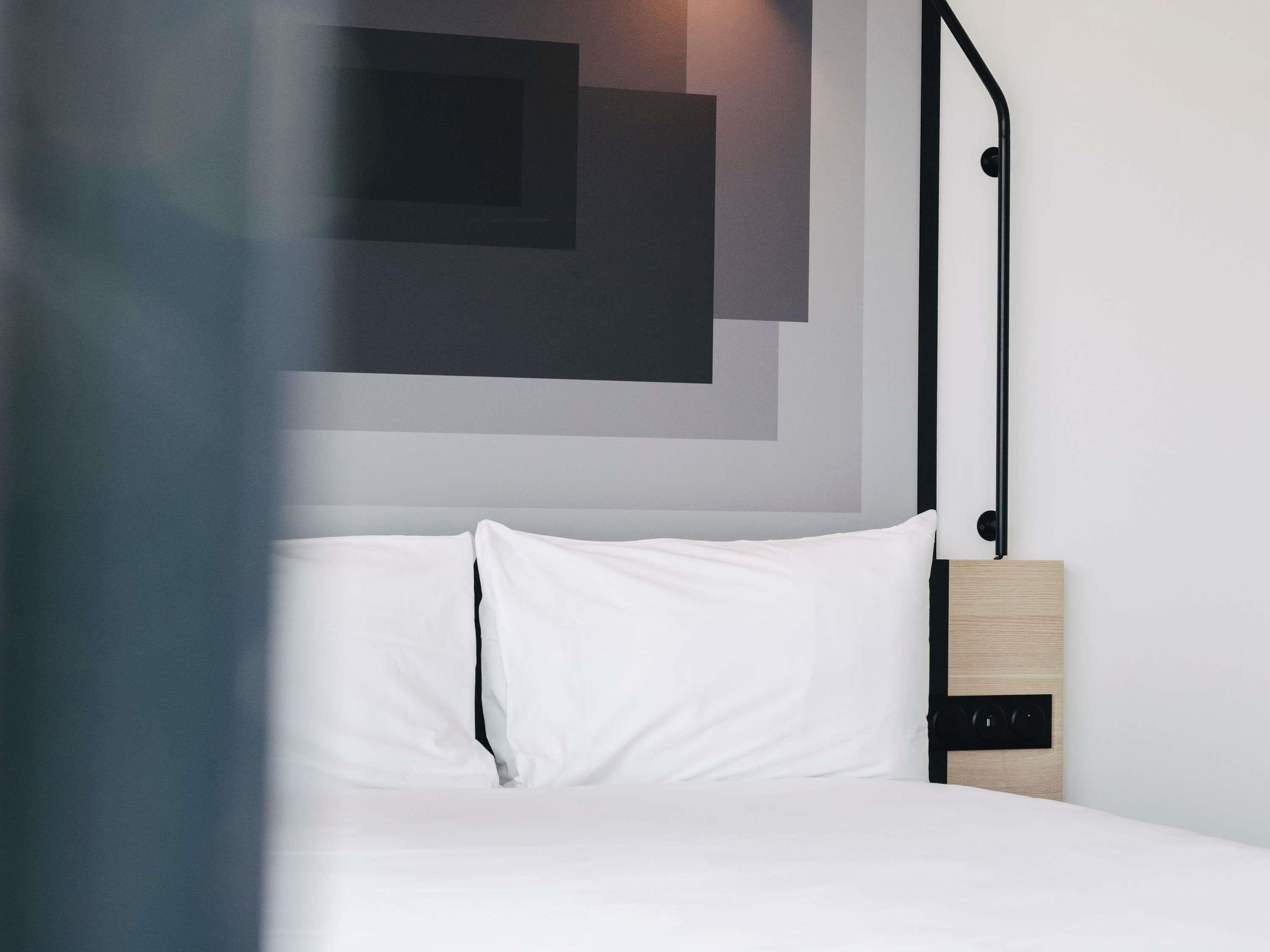 Een bed met witte beddengoed, een hoofdbord met een zwart metalen frame en een wandlamp.