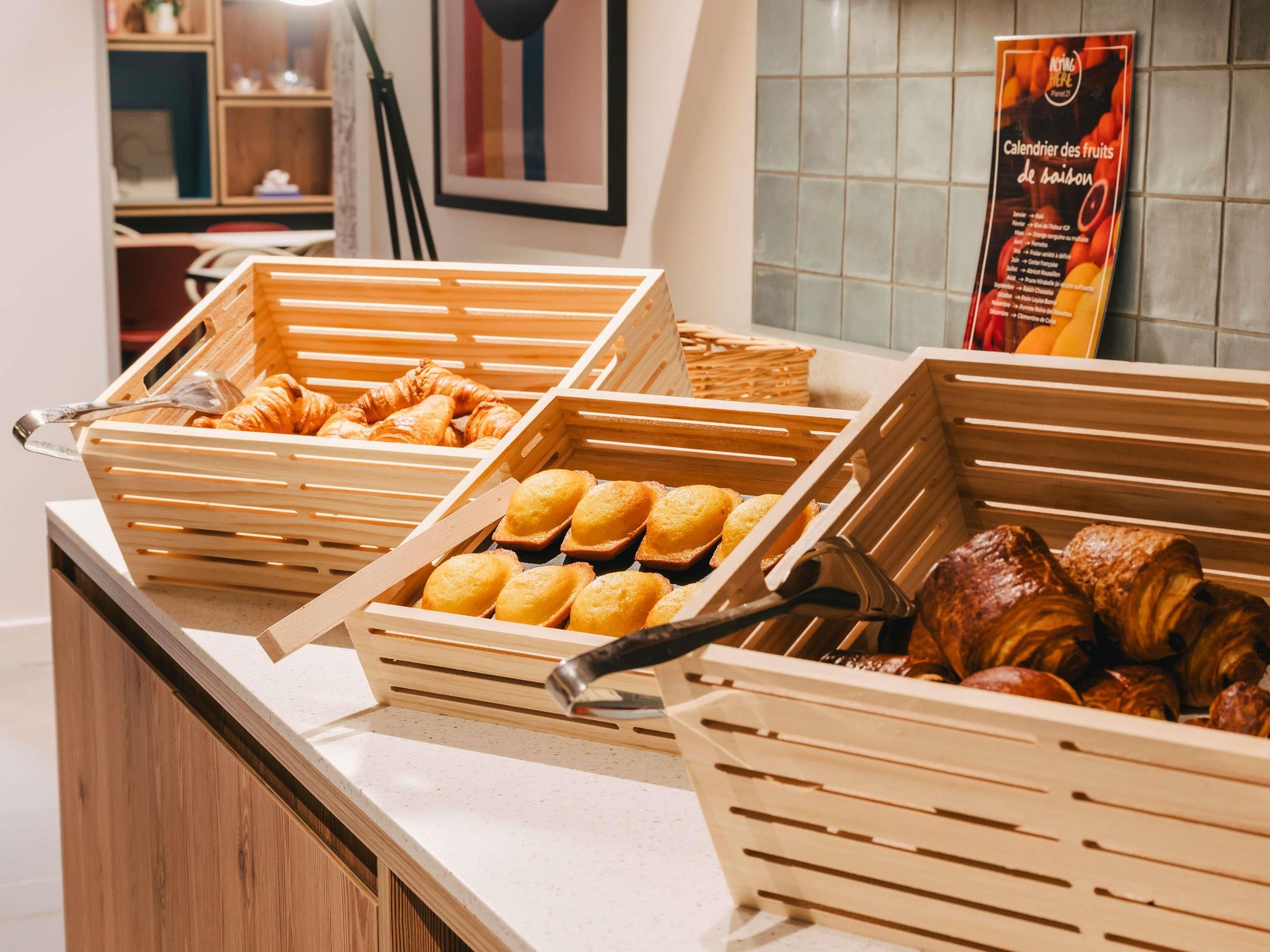 A breakfast buffet with wooden serving trays containing croissants, muffins, and pastries.