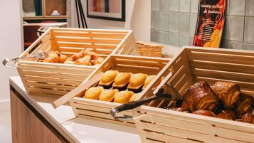 A breakfast buffet with wooden serving trays containing croissants, muffins, and pastries.