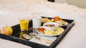 Una bandeja de desayuno ordenada con un vaso de jugo de naranja, un tazón de cereal, croissants y un plato de huevos sobre la cama en una habitación de hotel.