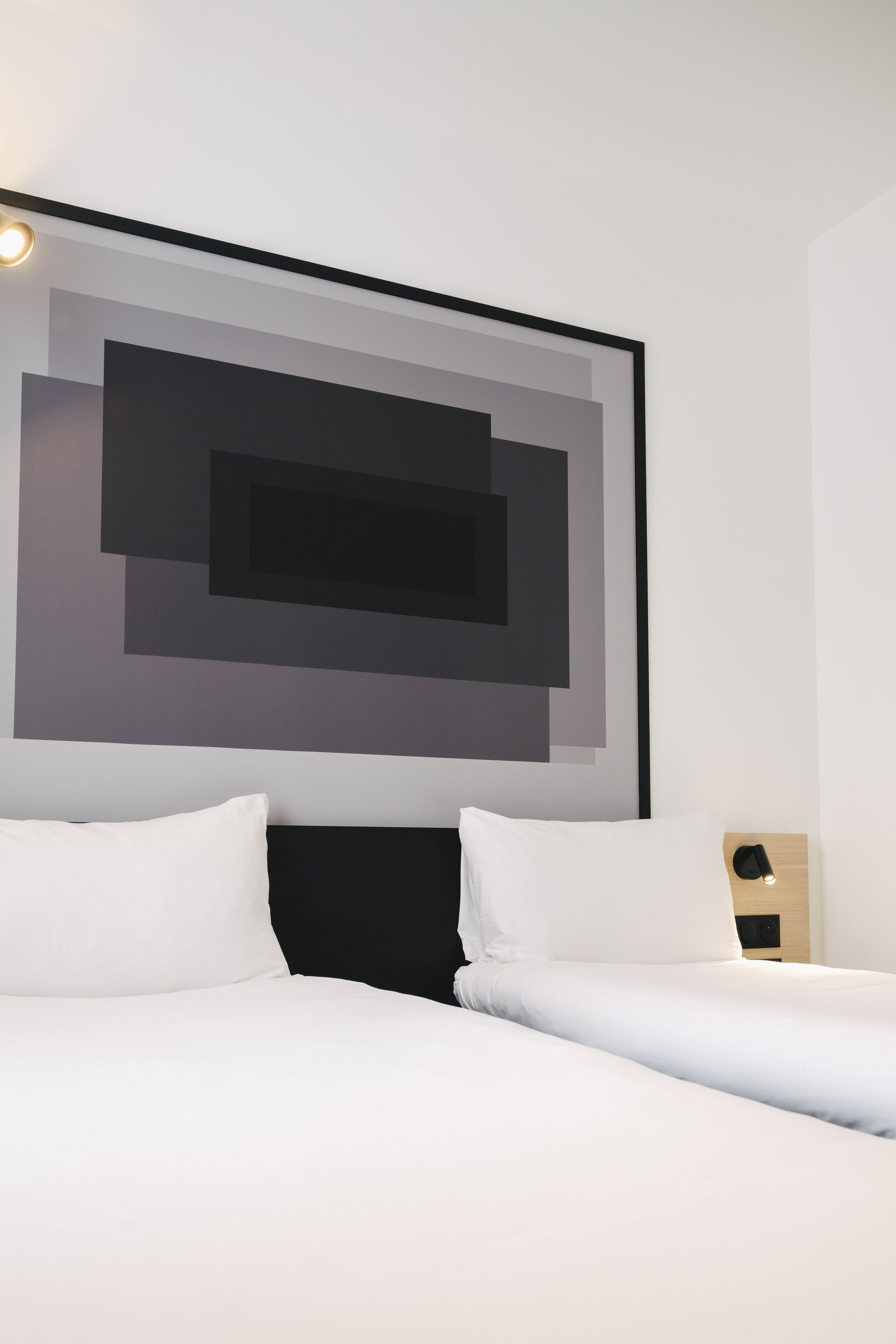Une chambre d’hôtel moderne avec une grande œuvre d’art abstraite accrochée au mur, un lit soigneusement fait avec du linge de lit blanc et une table de chevet en bois avec une lampe.