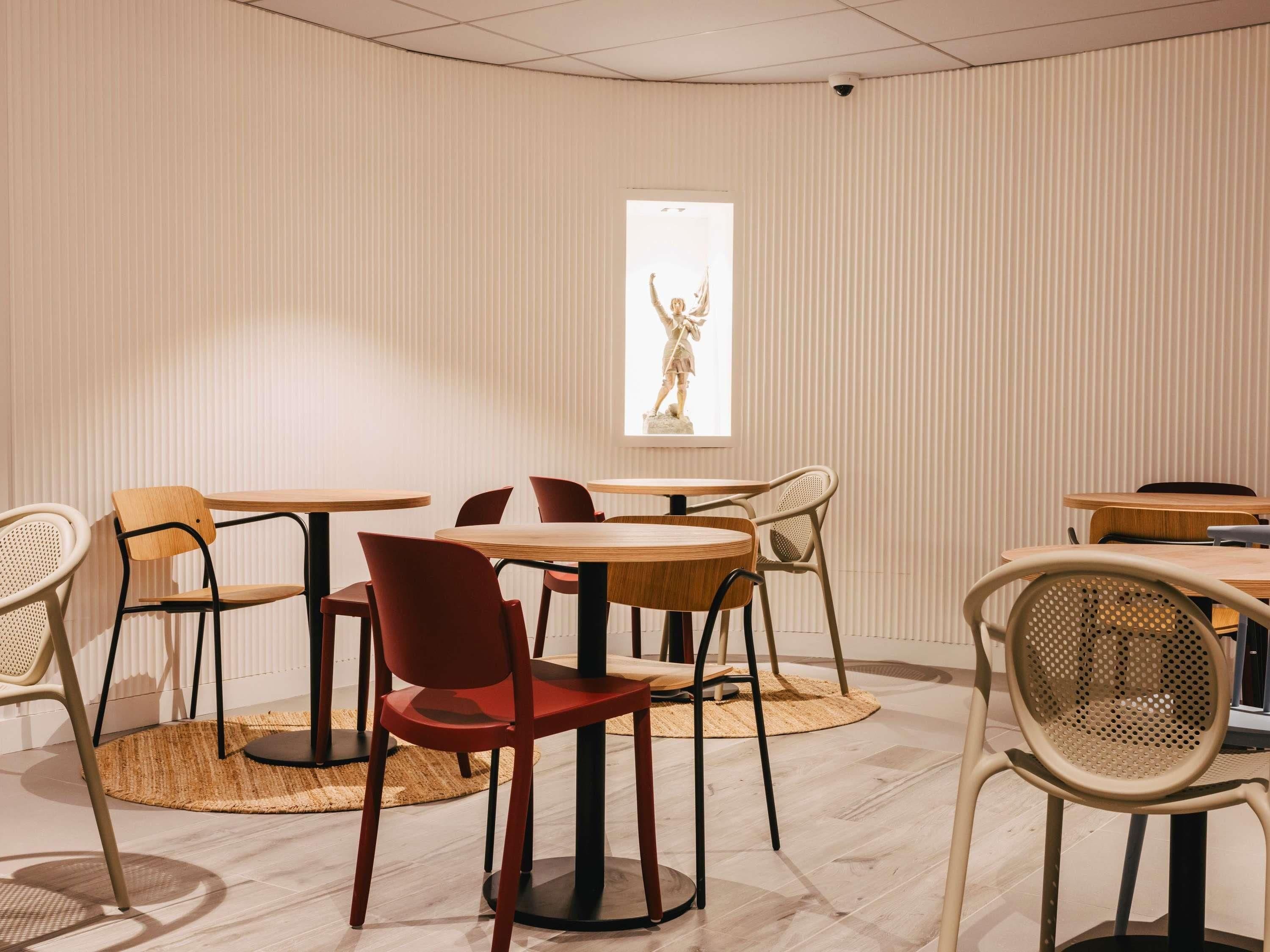 Un comedor moderno con mesas y sillas redondas, una estatua en la pared y un suelo con diseño.