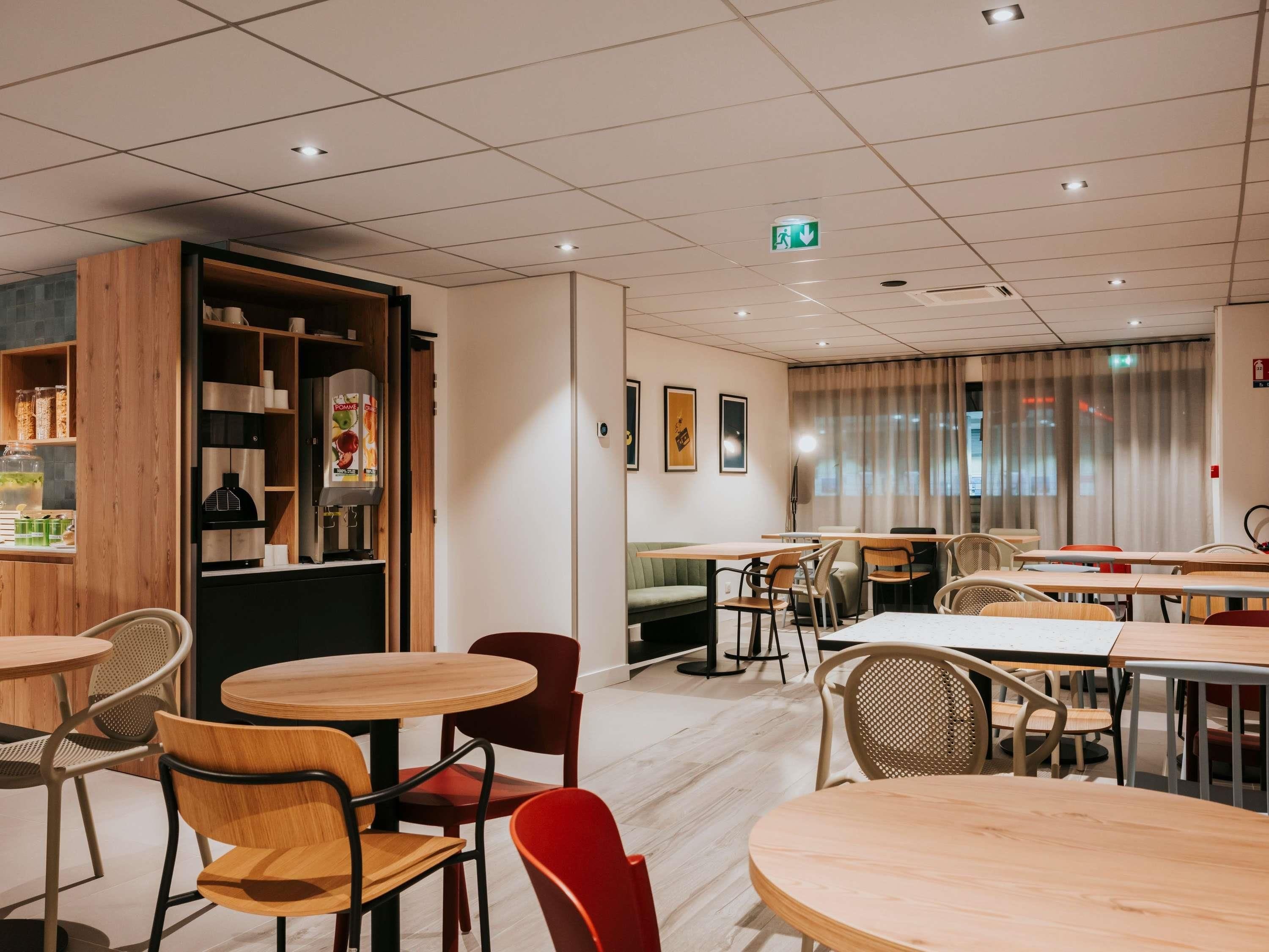 A modern cafe with round tables and chairs, a wooden bookshelf, and a large window with curtains.