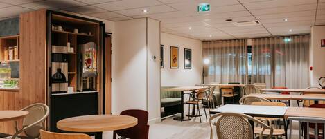 A modern cafe with round tables and chairs, a wooden bookshelf, and a large window with curtains.