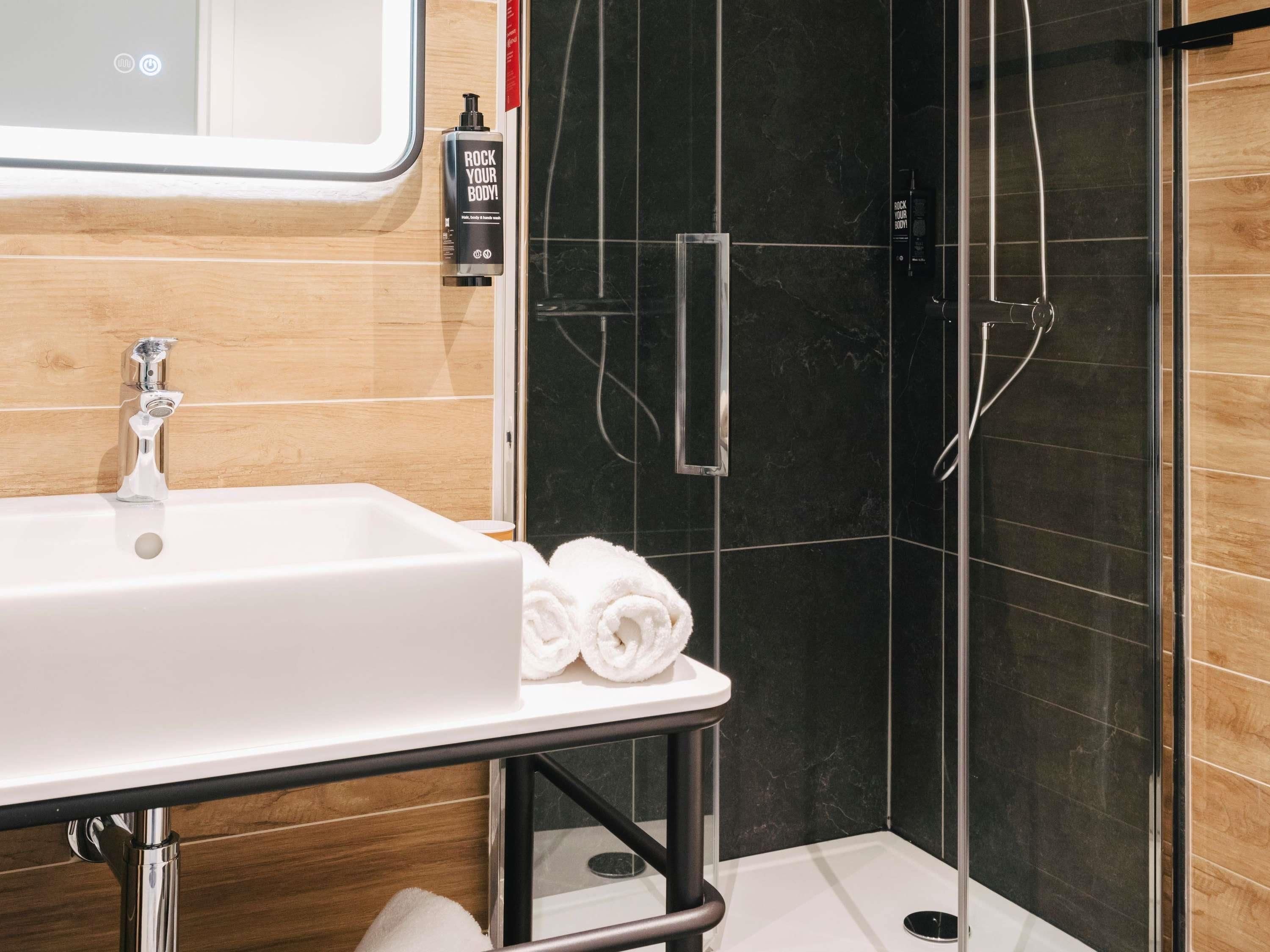 A modern bathroom with a white sink, a mirror, and a shower area with black tiles.