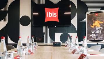 A conference room with a large screen displaying the ibis logo, a meeting table with name cards, and water bottles.
