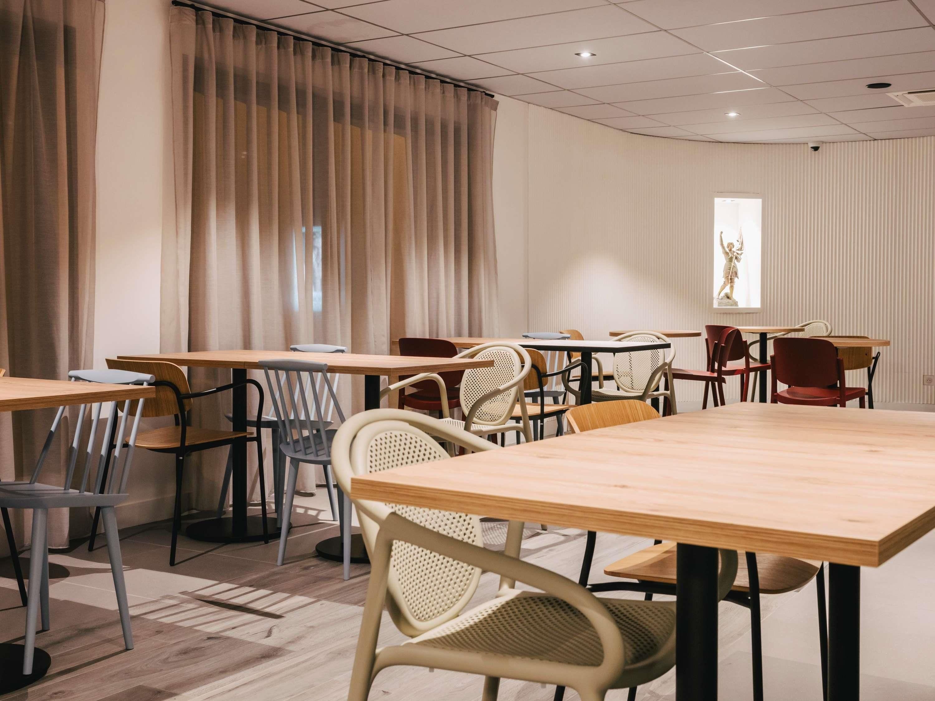 A conference room with multiple tables and chairs, a large window with curtains, and a statue on the wall.
