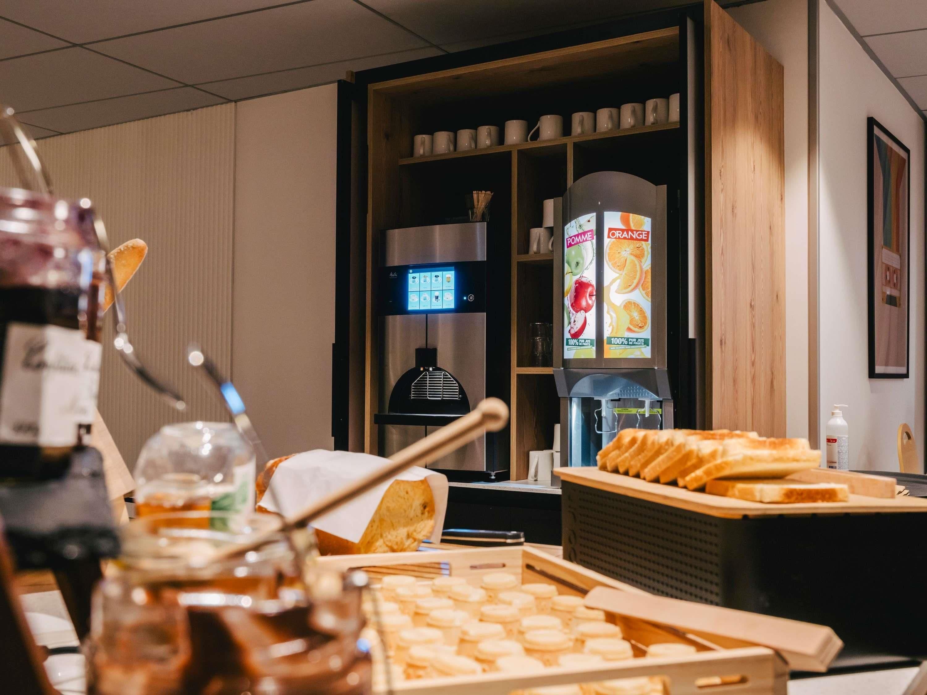 Un comptoir pour le petit-déjeuner avec des viennoiseries, une machine à café et un distributeur de jus.