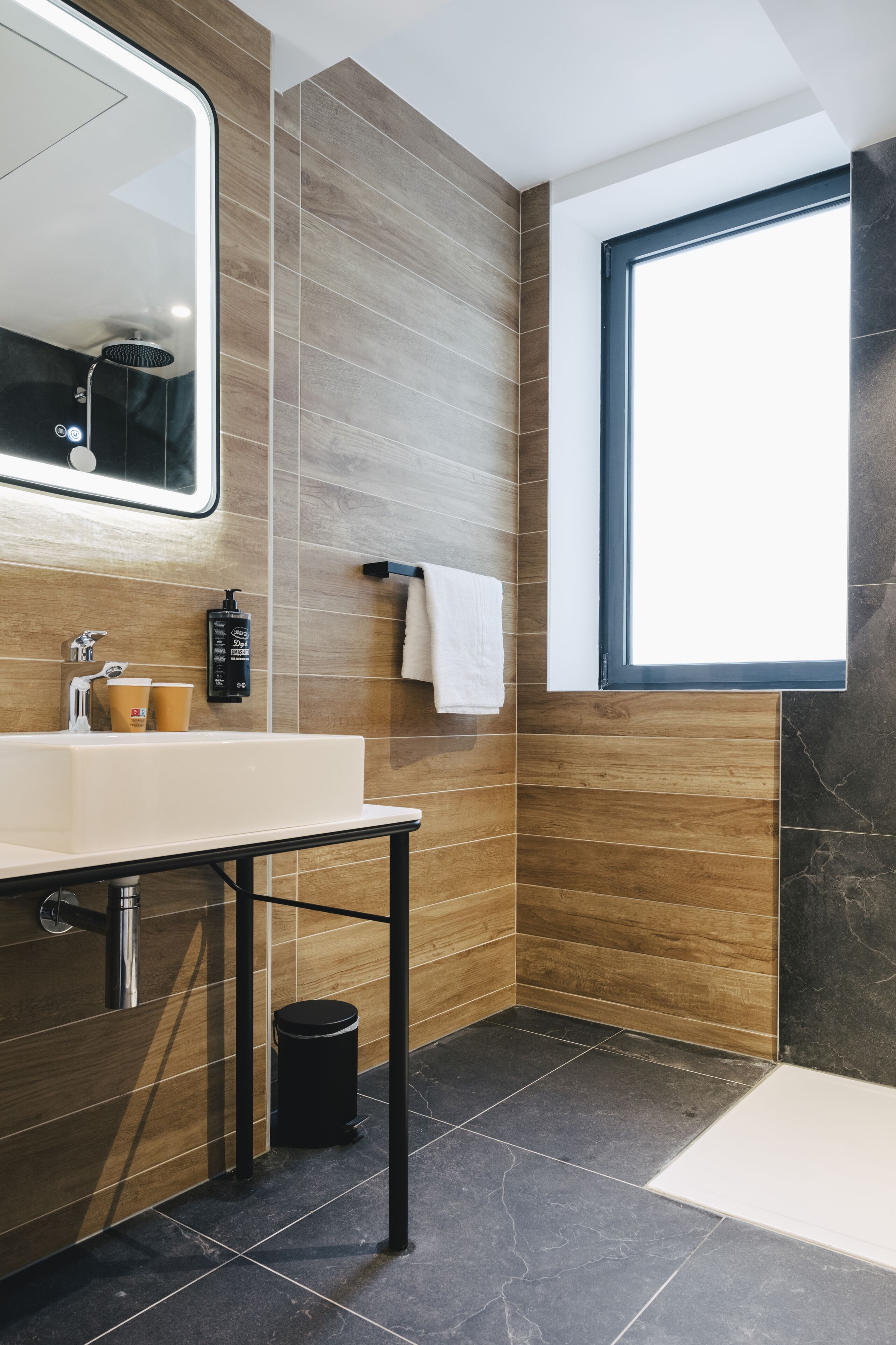 A modern bathroom with a large mirror, a sink, and a window.