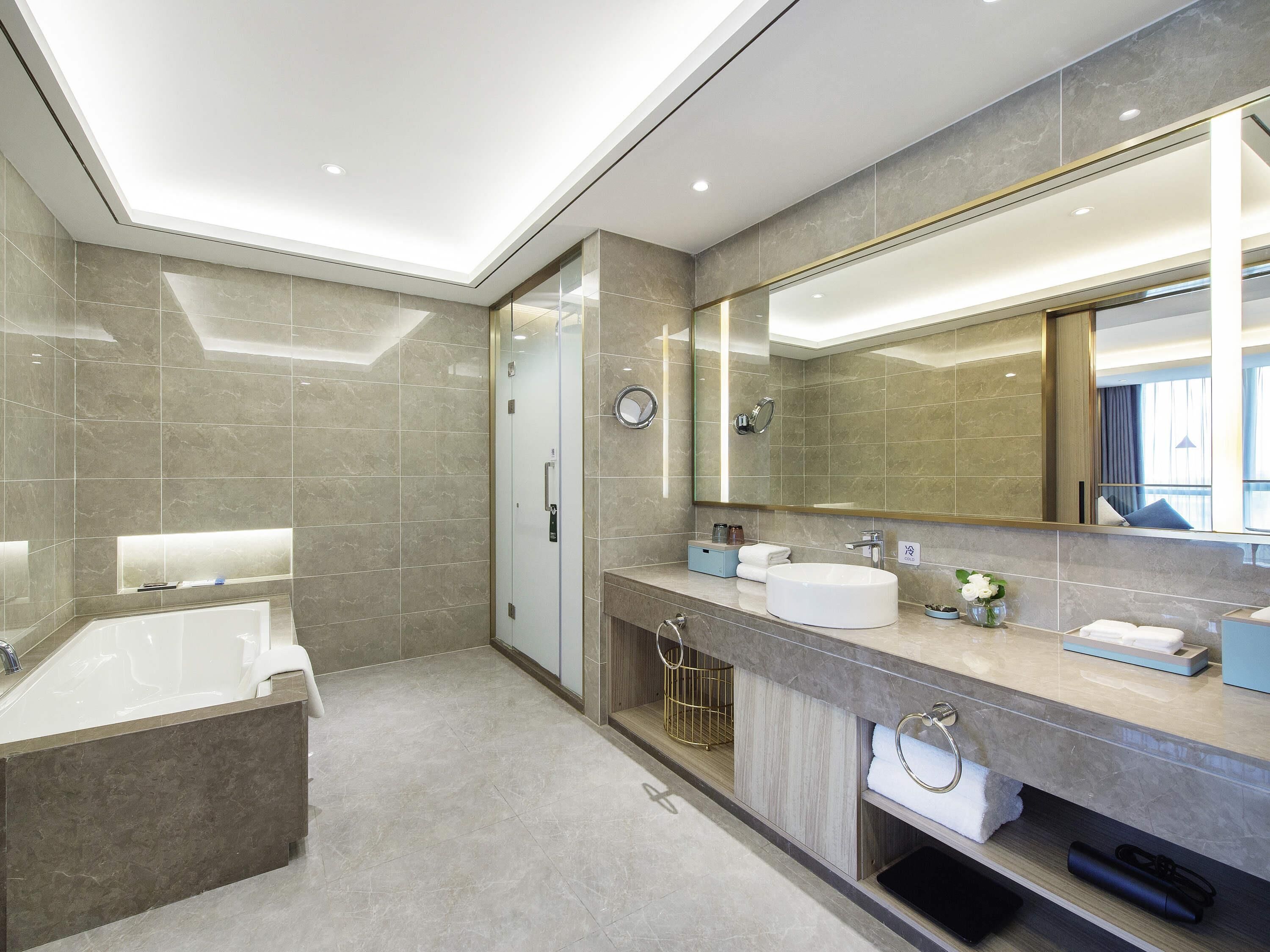 A modern bathroom with a bathtub, a large mirror, and a vanity with a sink.