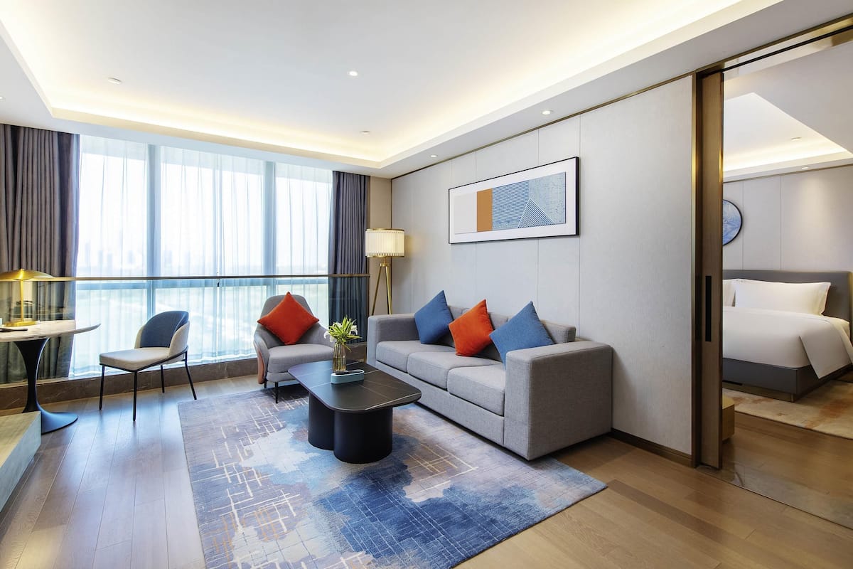 Een moderne hotelkamer met een bank, fauteuils, een salontafel, een bureau en een bed.