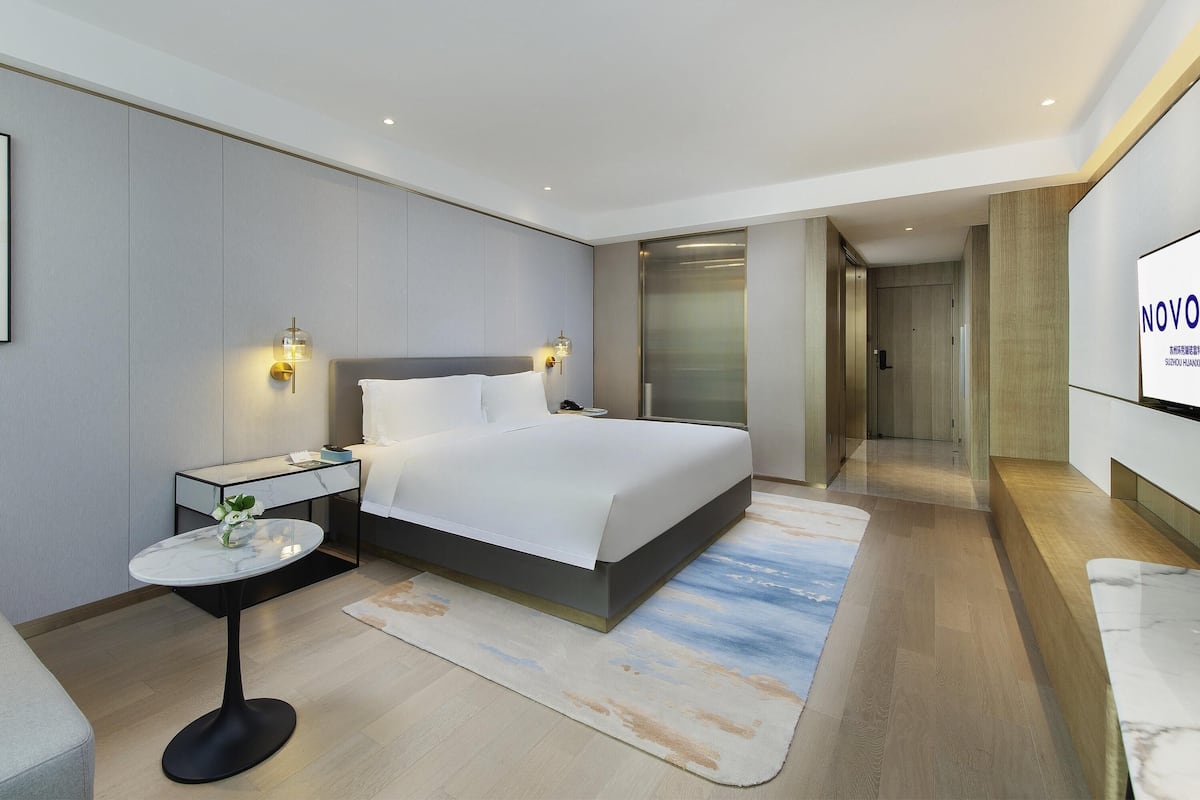 Een moderne hotelkamer met een groot bed, nachtkastjes, een klein rond tafeltje met een vaas en een televisie aan de muur.