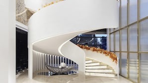 Una escalera espiral moderna con interior blanco, un área de descanso con superficie reflectante y vistas al exterior a través de amplias ventanas.