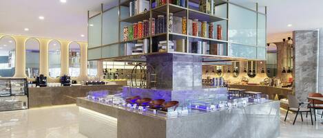 A modern hotel lobby with a central bar area, a marble reception desk, and a glass display case.