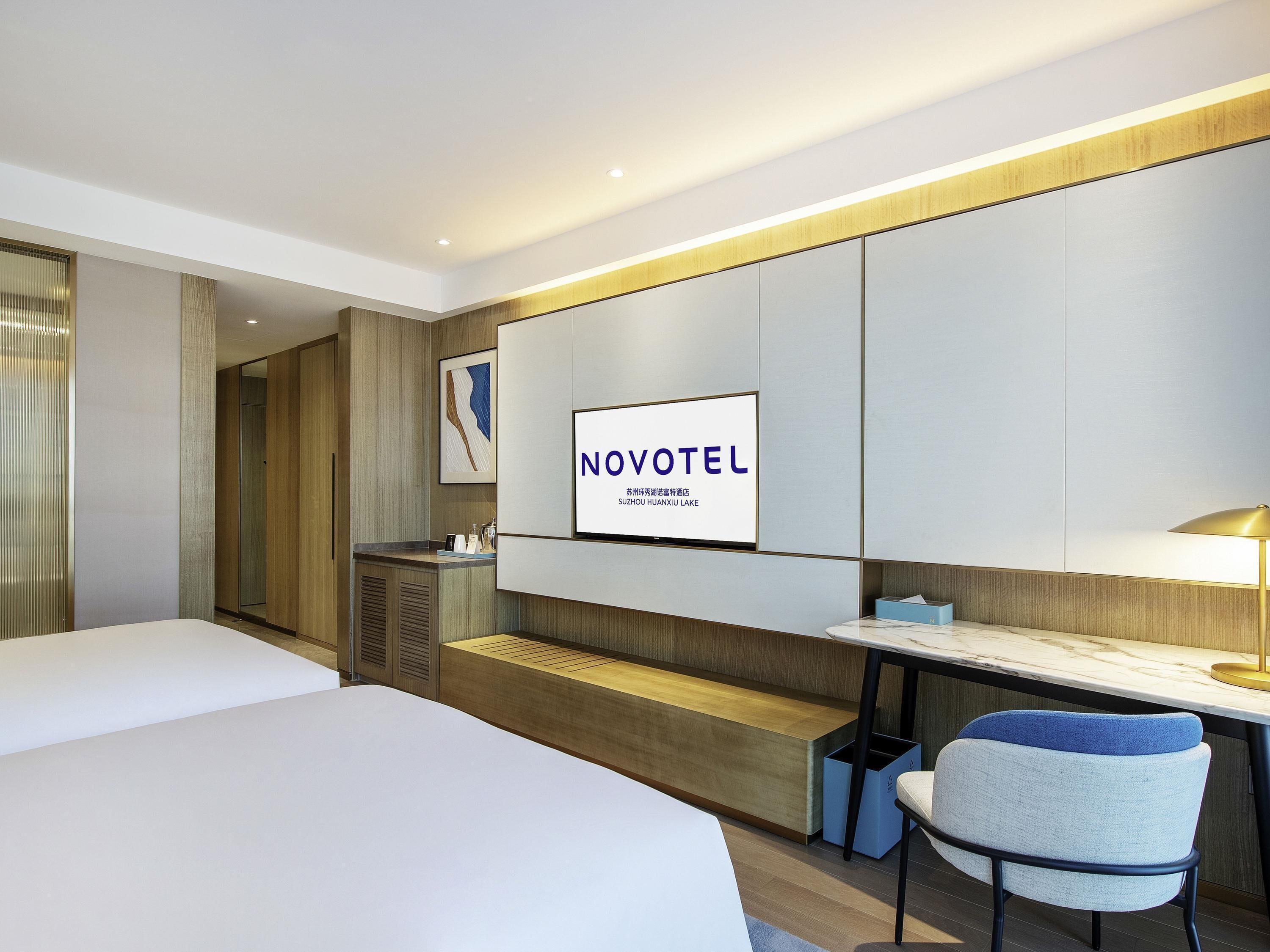 A modern hotel room with a bed, a desk, a chair, a TV, and a bench.