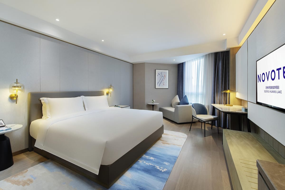 Een moderne hotelkamer met een groot bed, een bureau, een stoel en een televisiescherm waarop 'NOVOTE' staat.