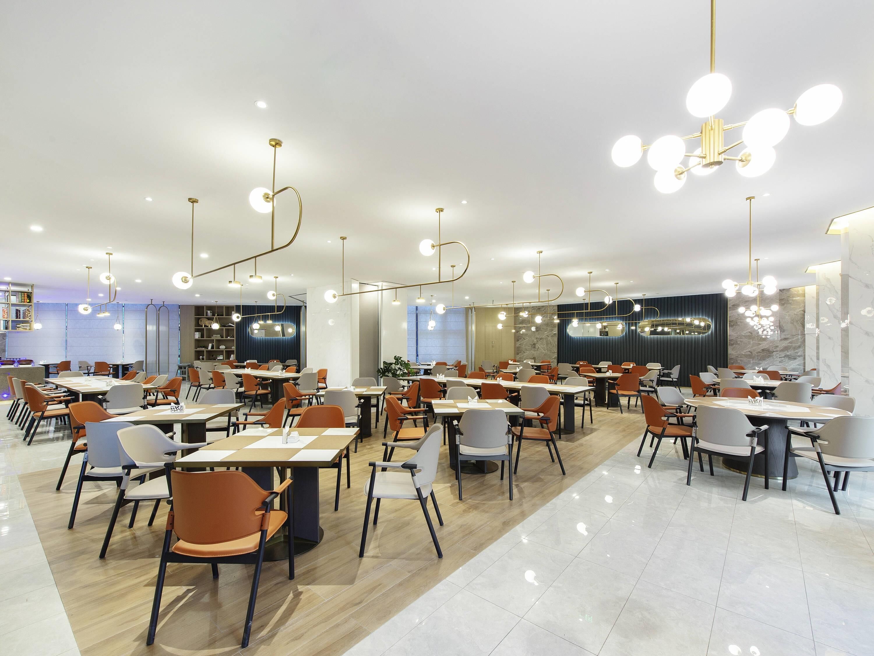 A modern dining area with multiple tables and chairs, overhead lighting fixtures, and a marble floor.