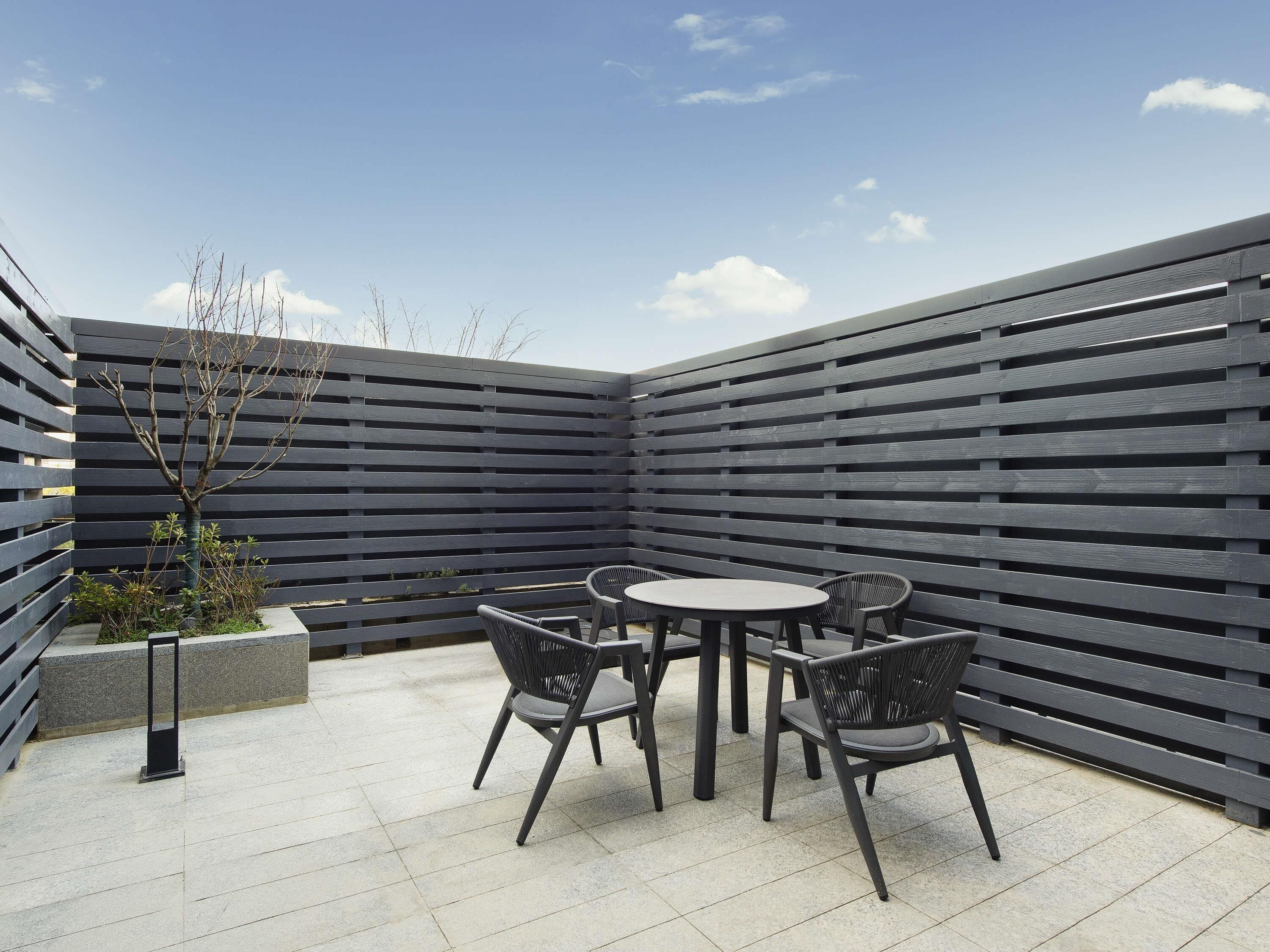 A patio with a round table and chairs, a black fence, and a small tree.