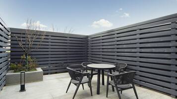 A patio with a round table and chairs, a black fence, and a small tree.
