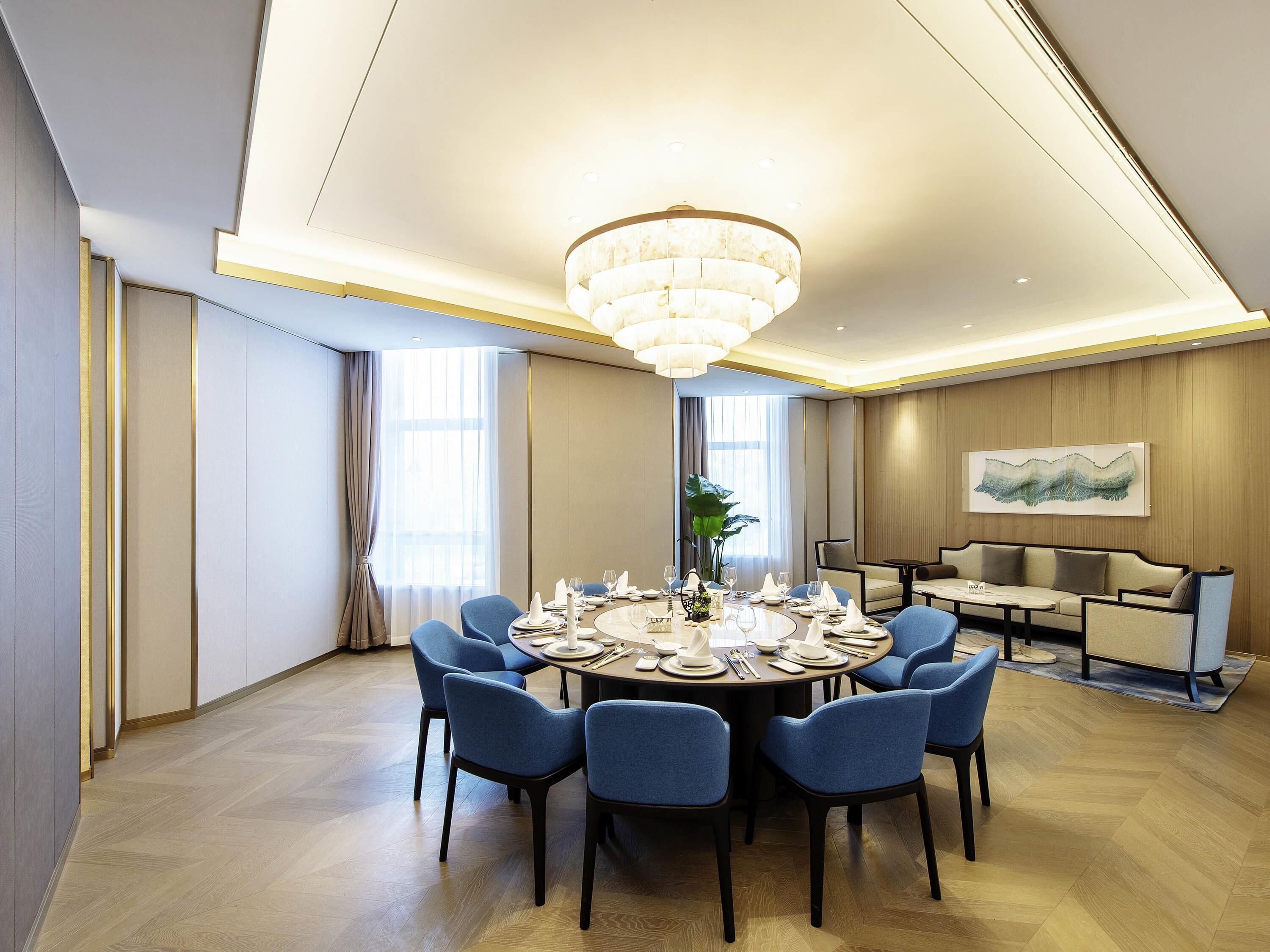 Comedor moderno con una mesa redonda preparada para seis personas, rodeada de sillas azules.
