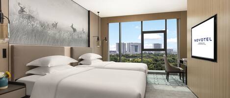A hotel room with two beds, a large window with a city view, a painting on the wall, and a sign reading 'NOVOTEL'.