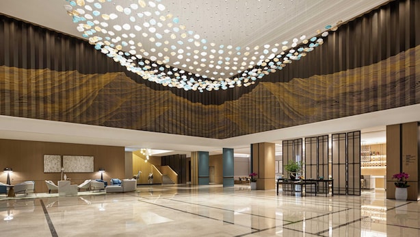 A spacious lobby with a modern chandelier, seating area, and a staircase. - Novotel Yancheng Exhibition Center (Yancheng)