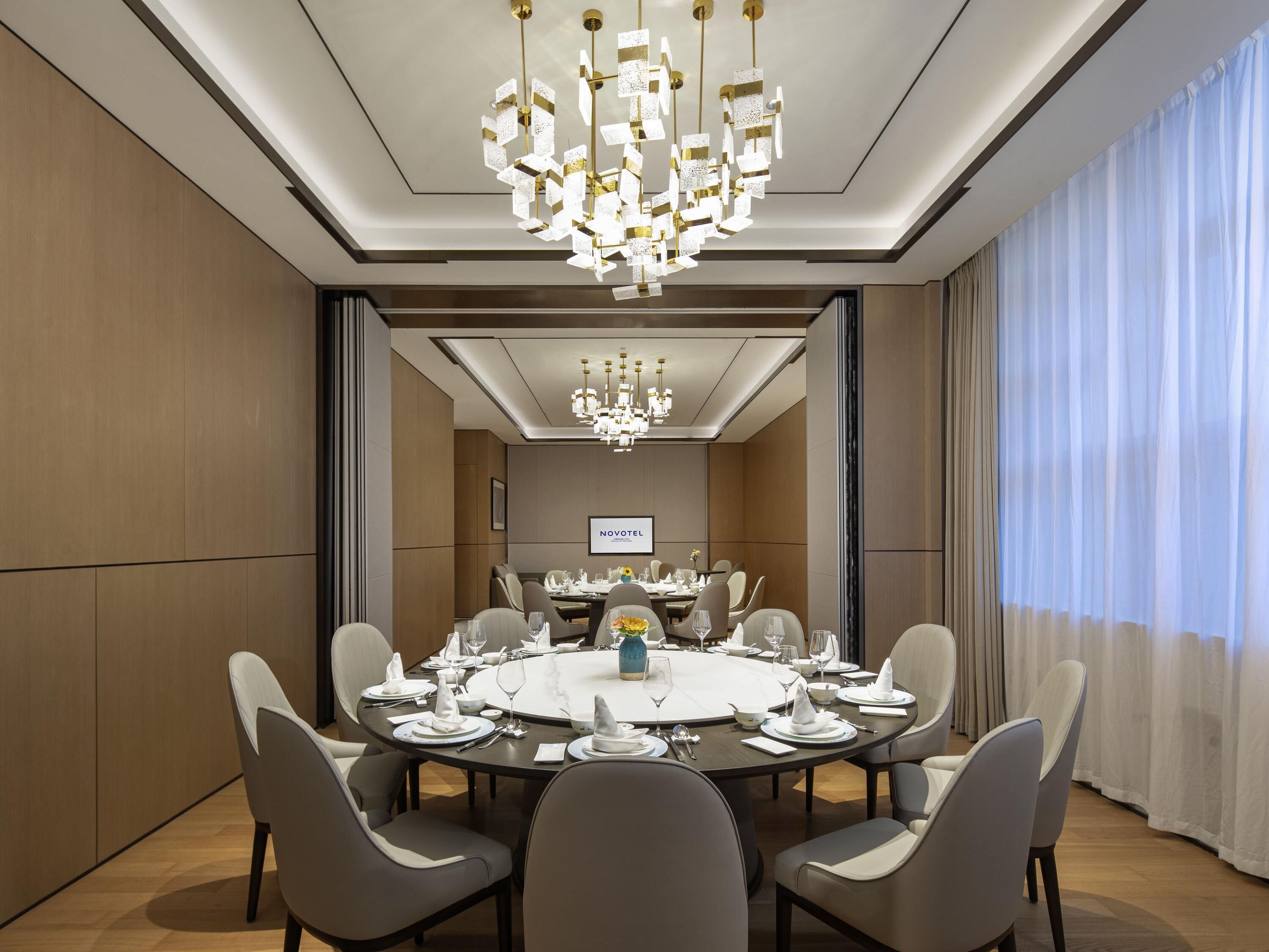 A conference room with a round table, chairs, a chandelier, and a television screen.