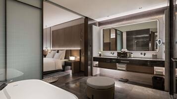 A modern bathroom with a large bathtub, a round vanity with a mirror, and a separate bedroom area with a bed and nightstands.