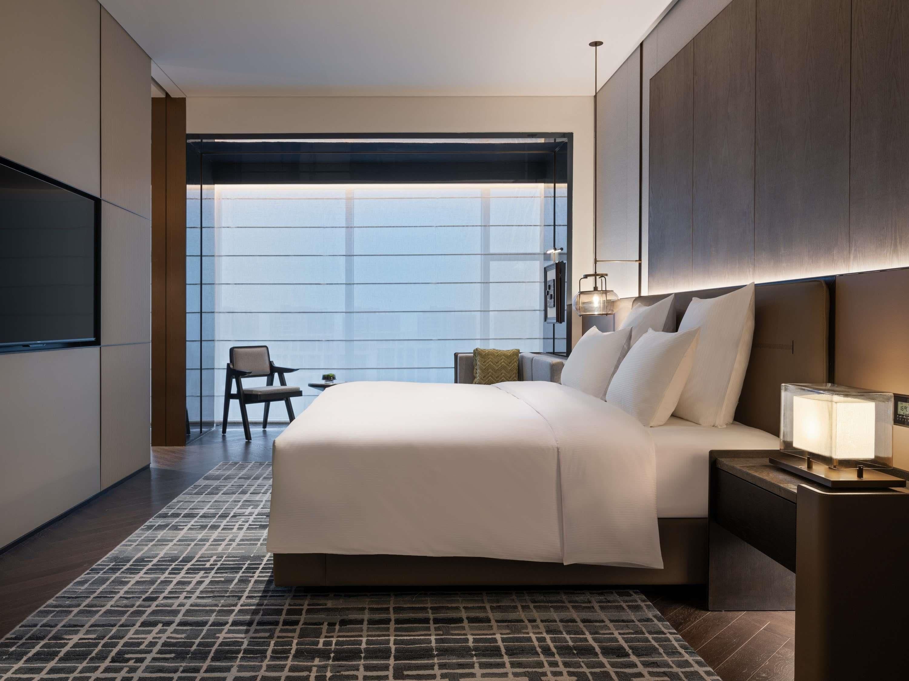 A modern hotel room with a large bed, a TV, a desk, and a chair.