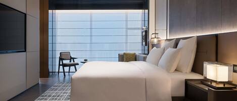 A modern hotel room with a large bed, a TV, a desk, and a chair.