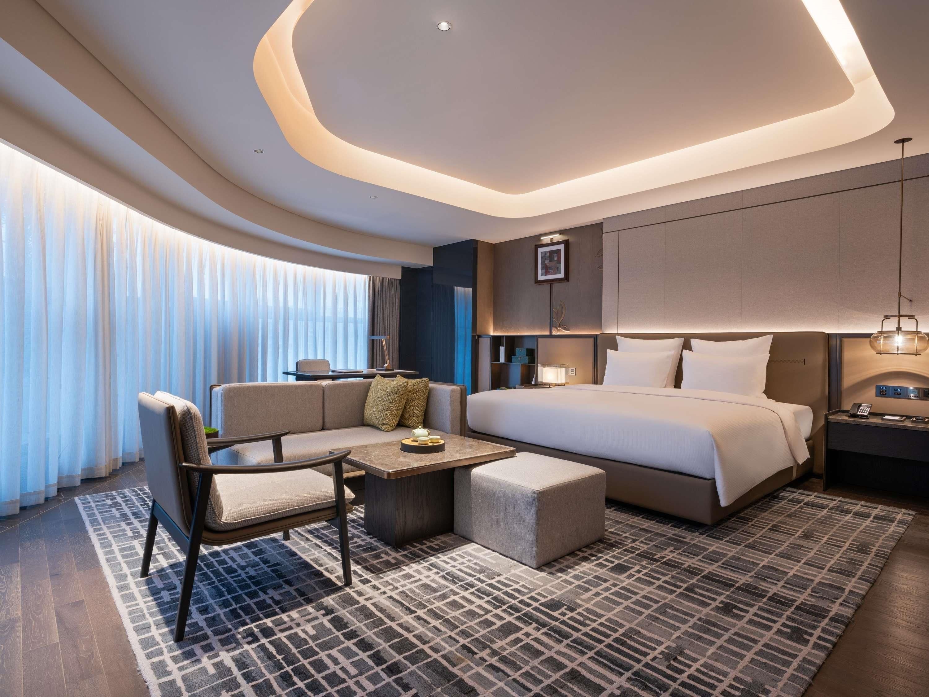 Una habitación de hotel moderna con una cama grande, un sofá, una mesita y un escritorio.