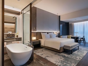 Una habitación de hotel moderna con una cama grande, una sala de estar separada, una bañera y un espejo amplio.