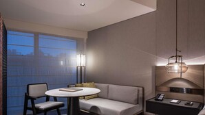 A modern hotel room with a round table, two chairs, a sofa, a nightstand with a lamp, and a view of the city through large windows. - Pullman Quanzhou Shuitou (Quanzhou)