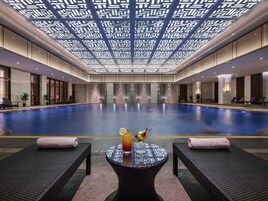 Una amplia piscina interior con sillones de descanso y una mesa con bebida y fruta.