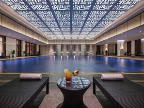 Una amplia piscina interior con sillones de descanso y una mesa con bebida y fruta.