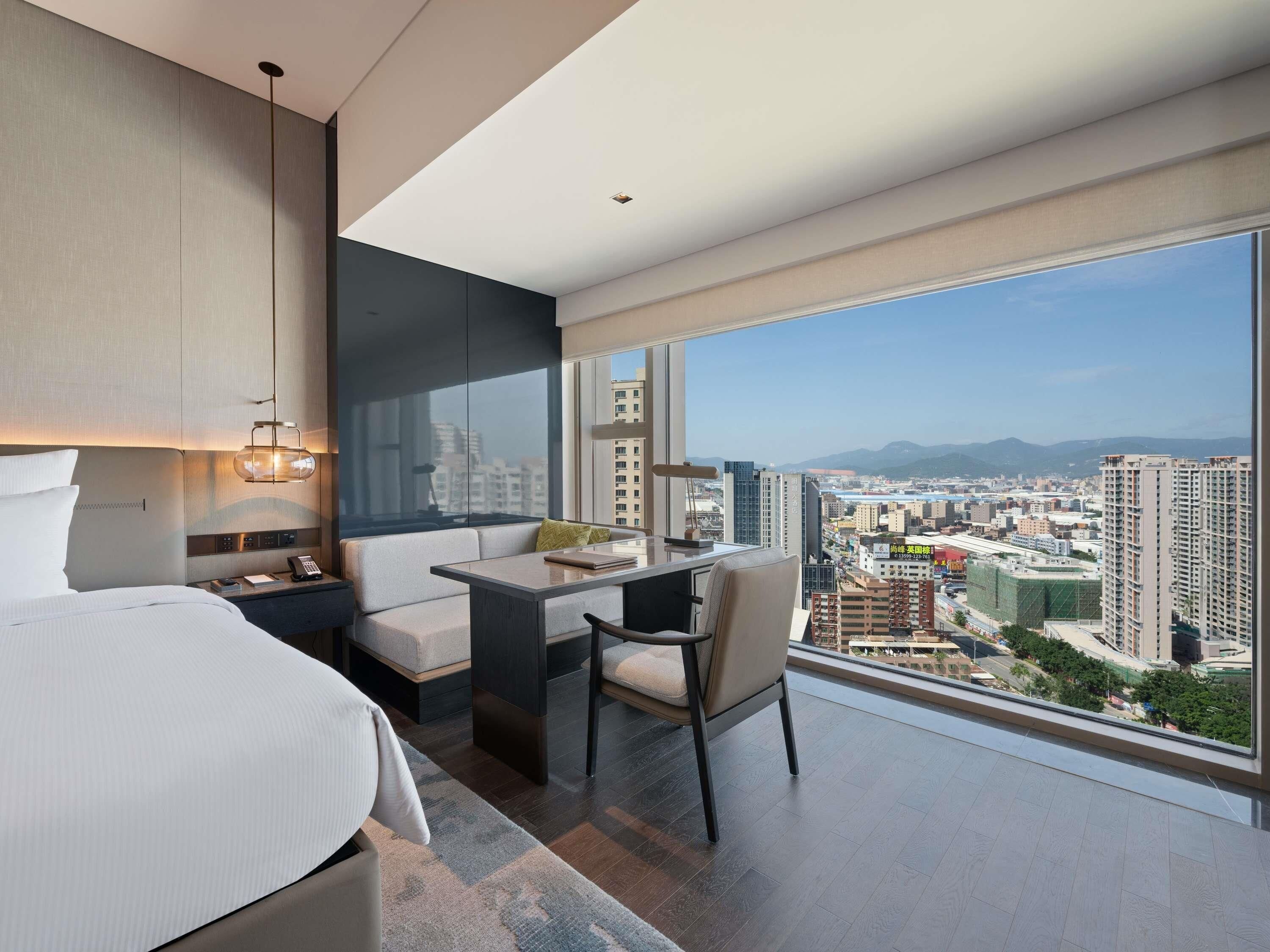 Una habitación de hotel moderna con una cama, un escritorio y vistas a la ciudad.