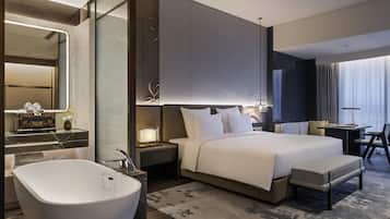 A modern hotel room with a large bed, a separate sitting area, a large bathroom with a freestanding bathtub, and a large mirror.